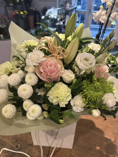 Blush Whisper Elegance - A soft and romantic arrangement that exudes grace and timeless charm. Gentle blush tones are nestled among creamy whites and fresh greenery, creating a delicate balance of warmth and freshness. The layered textures and natural flow give this piece an effortlessly elegant, garden-inspired feel, while subtle structural accents add a modern touch. Perfect for meaningful moments or refined gifting, this design offers a beautiful expression of tenderness and sophistication.